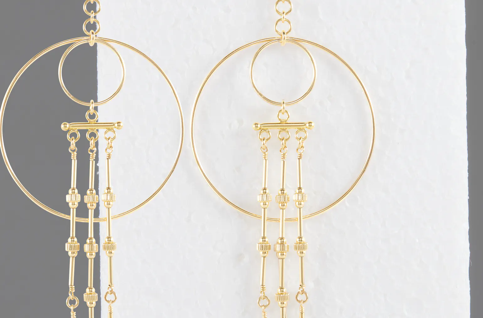 Gold drop earrings photographed against a textured wall